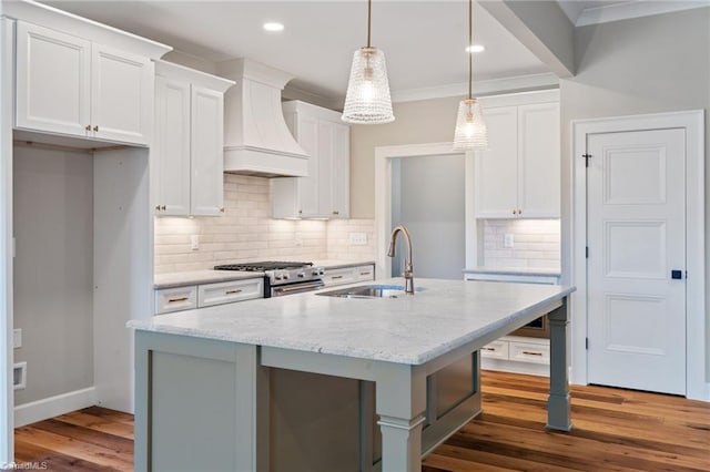 kitchen featuring premium range hood, dark wood-type flooring, a center island with sink, a sink, and stainless steel range with gas stovetop