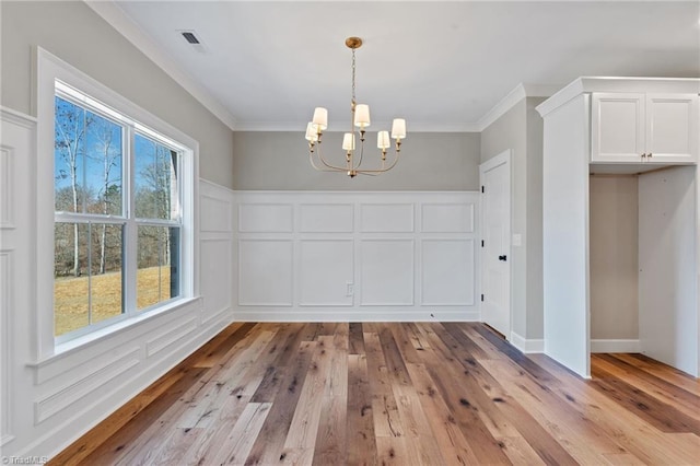 unfurnished dining area featuring visible vents, a notable chandelier, light wood-style floors, crown molding, and a decorative wall