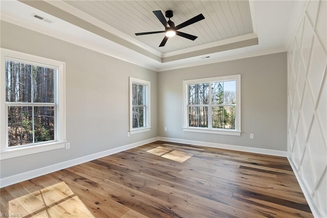 empty room with hardwood / wood-style floors, visible vents, baseboards, ornamental molding, and a raised ceiling