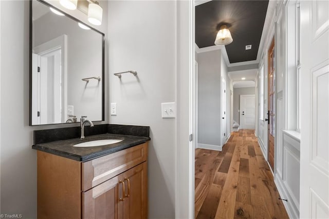 bathroom featuring vanity, crown molding, baseboards, and wood finished floors