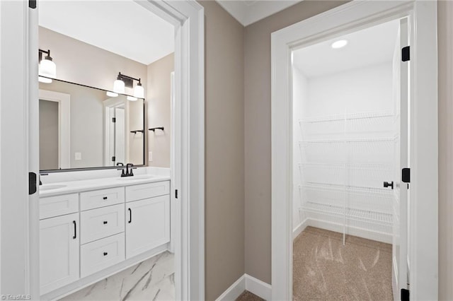 bathroom with baseboards, double vanity, a sink, a walk in closet, and marble finish floor