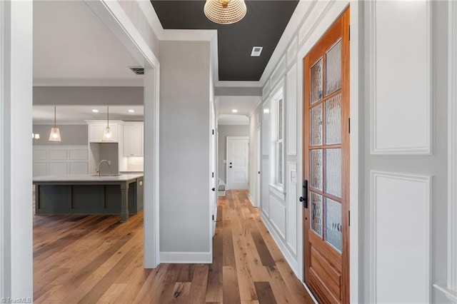 hallway with visible vents, light wood-type flooring, and ornamental molding