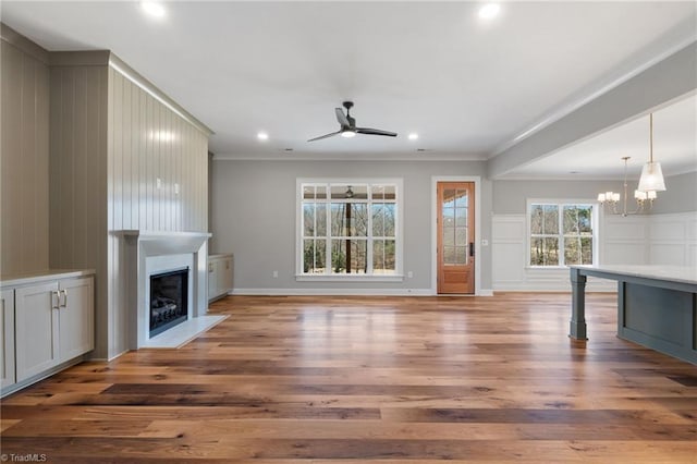 unfurnished living room featuring a fireplace with flush hearth, wood finished floors, crown molding, and ceiling fan with notable chandelier