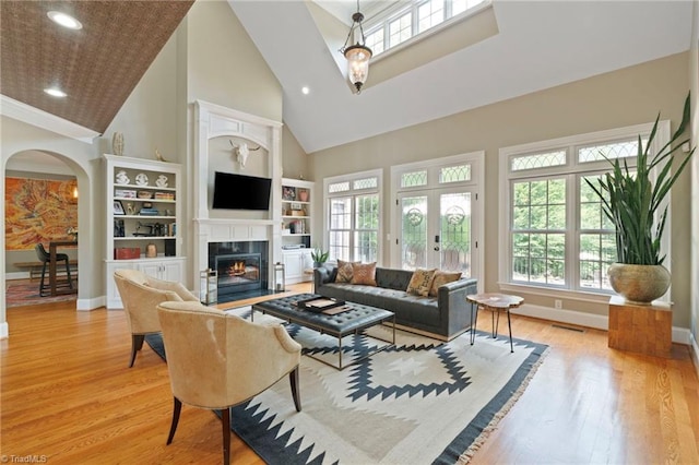 living room with built in features, light hardwood / wood-style flooring, and a towering ceiling