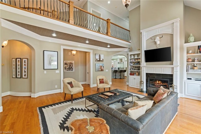 living room with light hardwood / wood-style floors, ornamental molding, a tiled fireplace, and a towering ceiling