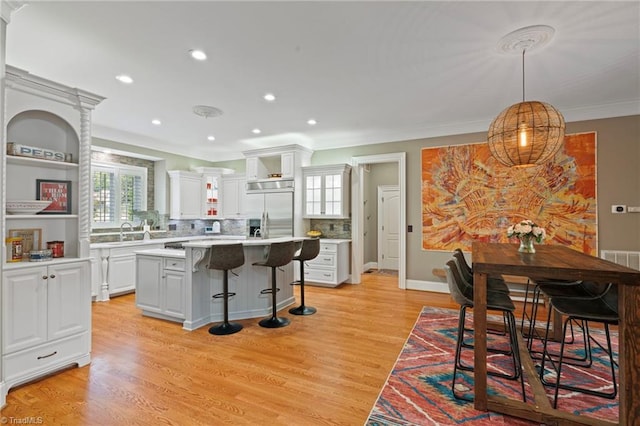 kitchen featuring light hardwood / wood-style flooring, backsplash, a center island, white cabinetry, and ornamental molding