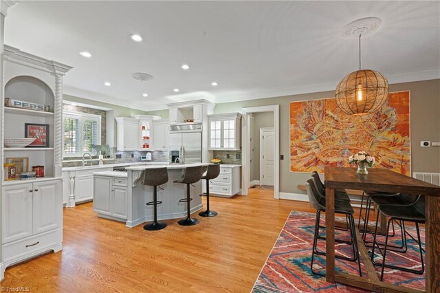 kitchen featuring light wood-type flooring, white cabinets, backsplash, stainless steel double oven, and a kitchen breakfast bar