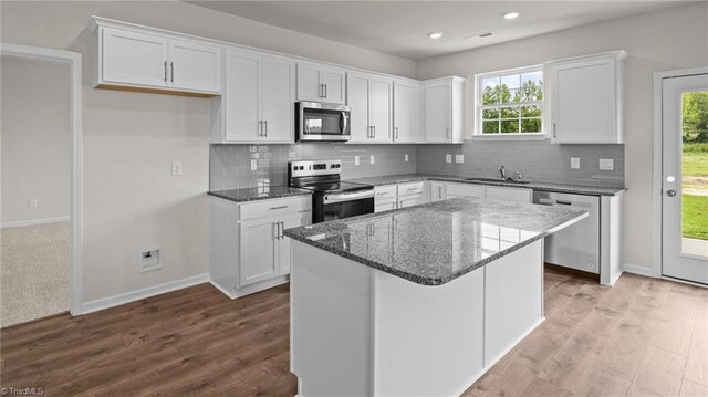 kitchen with a healthy amount of sunlight, dark stone countertops, stainless steel appliances, white cabinetry, and a sink