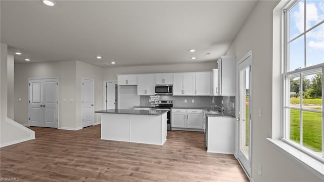 kitchen with a sink, appliances with stainless steel finishes, white cabinetry, backsplash, and a center island