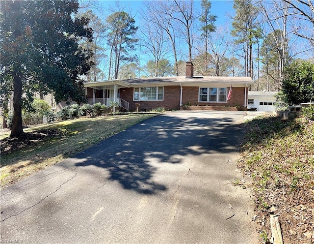 ranch-style house with aphalt driveway, brick siding, and a chimney