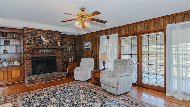 living room featuring wood walls, crown molding, hardwood / wood-style flooring, ceiling fan, and a fireplace