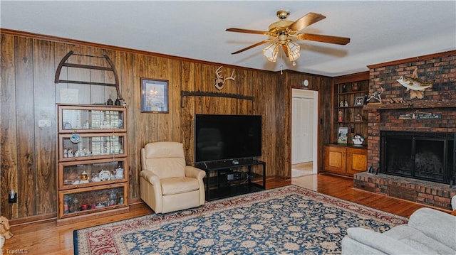 living room featuring crown molding, wooden walls, a brick fireplace, ceiling fan, and light hardwood / wood-style floors