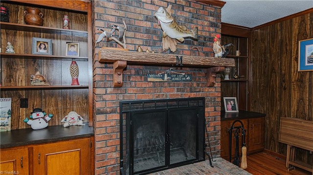living room featuring a brick fireplace, crown molding, hardwood / wood-style floors, a textured ceiling, and wooden walls