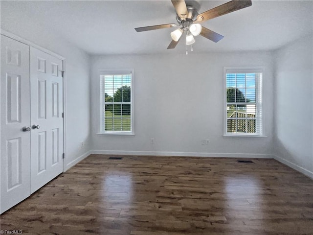 unfurnished bedroom with ceiling fan, multiple windows, a closet, and dark hardwood / wood-style flooring