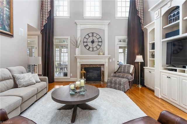 living room featuring light wood-style flooring, a towering ceiling, and a high end fireplace