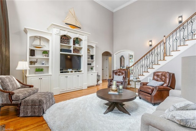 living area with stairway, wood finished floors, arched walkways, a towering ceiling, and crown molding