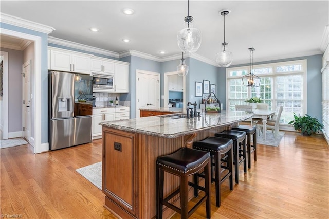 kitchen featuring a large island with sink, light wood-style floors, white cabinets, stainless steel appliances, and a sink