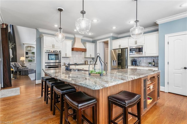 kitchen featuring light wood-type flooring, custom range hood, stainless steel appliances, white cabinetry, and a sink