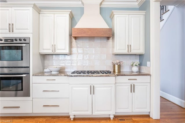 kitchen featuring light stone countertops, premium range hood, backsplash, and stainless steel appliances