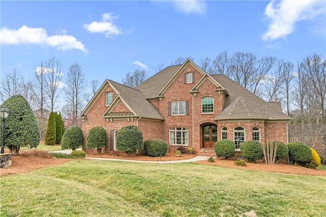 traditional-style house featuring brick siding, a front yard, and roof with shingles