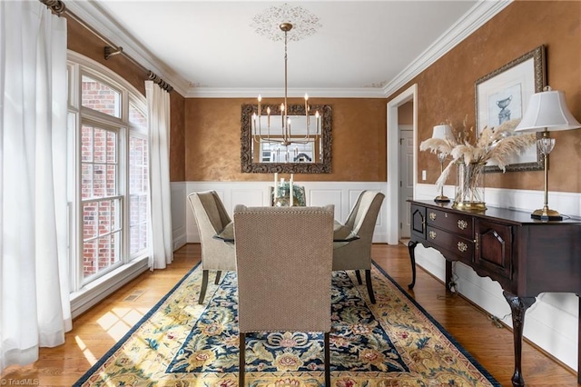 dining room featuring a notable chandelier, a wainscoted wall, light wood-style flooring, and ornamental molding