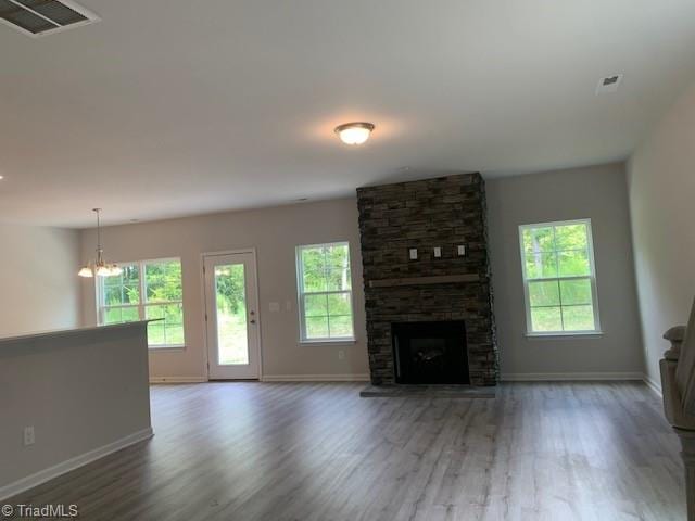 unfurnished living room featuring a stone fireplace, hardwood / wood-style flooring, a notable chandelier, and a healthy amount of sunlight