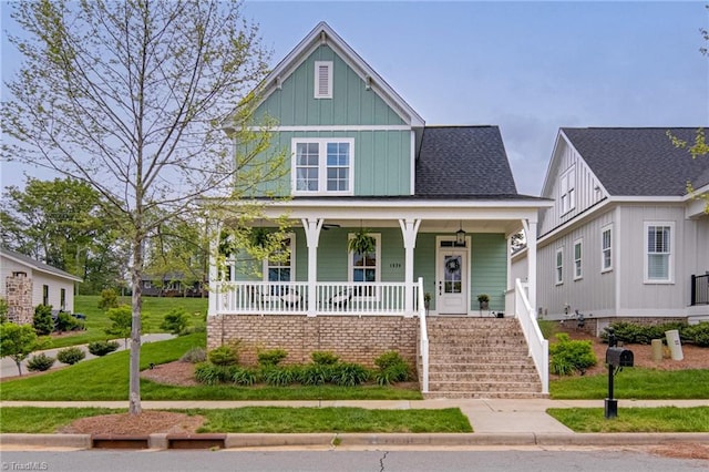view of front facade with board and batten siding, a front lawn, covered porch, and stairway