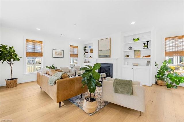 living room with recessed lighting, a glass covered fireplace, light wood-type flooring, and plenty of natural light