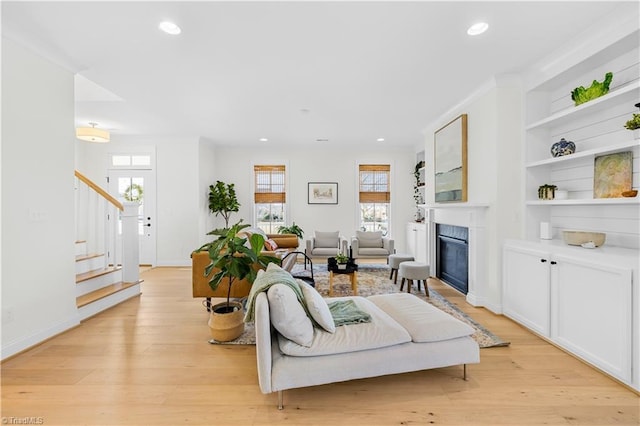 living area with recessed lighting, a glass covered fireplace, stairway, and light wood-type flooring