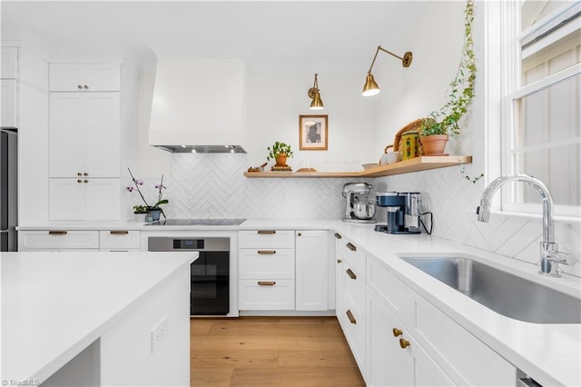 kitchen featuring black electric cooktop, oven, a sink, open shelves, and premium range hood