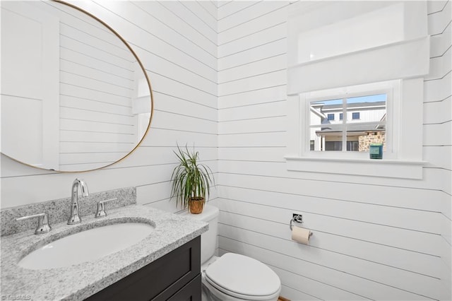 half bath featuring wooden walls, toilet, and vanity