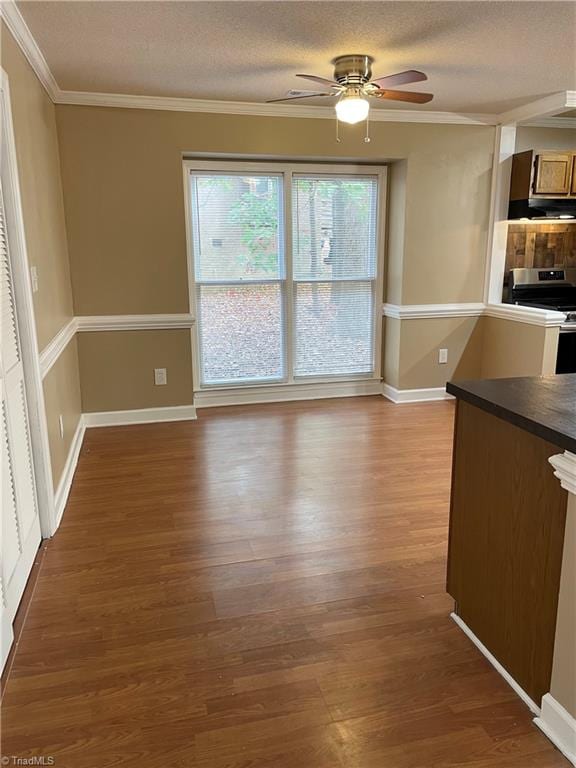 unfurnished dining area featuring ornamental molding, dark wood-type flooring, a textured ceiling, and ceiling fan