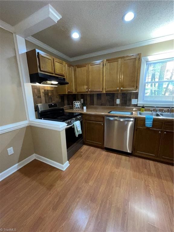 kitchen with light wood-type flooring, a textured ceiling, ornamental molding, and stainless steel appliances