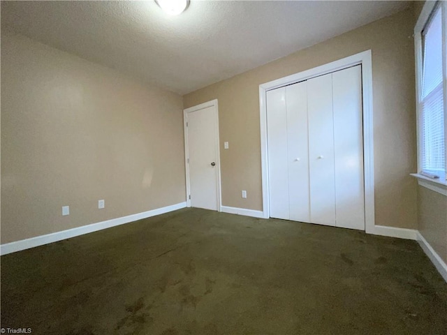 unfurnished bedroom with a textured ceiling, a closet, and dark carpet