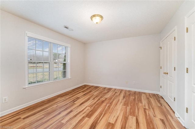 empty room featuring light wood-style floors, visible vents, a textured ceiling, and baseboards