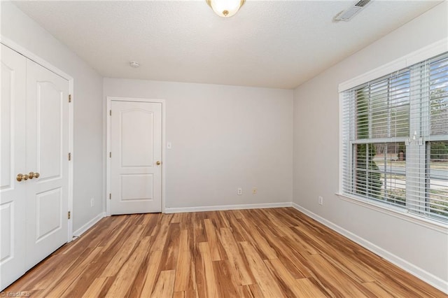 empty room featuring baseboards, visible vents, light wood finished floors, and a textured ceiling