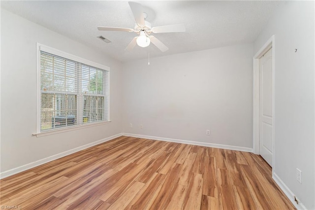 spare room with a textured ceiling, ceiling fan, visible vents, baseboards, and light wood finished floors