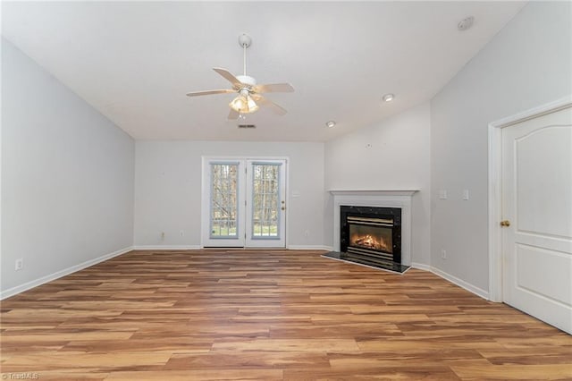 unfurnished living room with light wood-style floors, vaulted ceiling, baseboards, and a premium fireplace