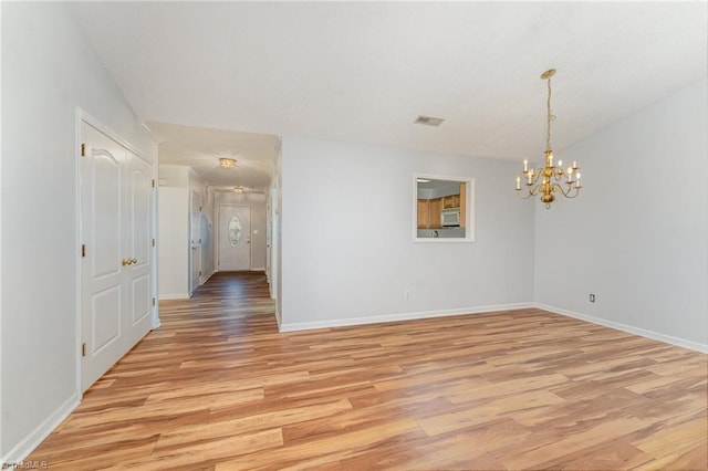 spare room with a chandelier, light wood finished floors, visible vents, and baseboards