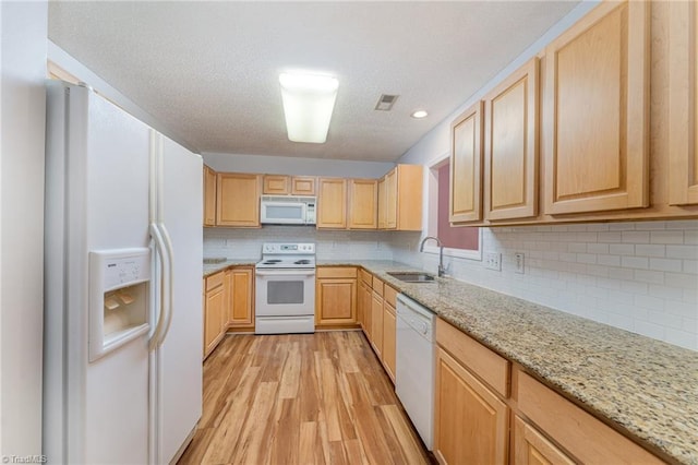 kitchen with tasteful backsplash, light wood-style floors, light brown cabinets, a sink, and white appliances