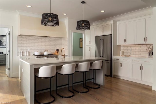 kitchen featuring a breakfast bar area, light wood finished floors, high end fridge, white cabinets, and crown molding