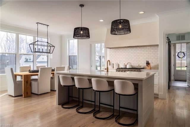 kitchen with tasteful backsplash, a breakfast bar area, light countertops, light wood-type flooring, and ornamental molding