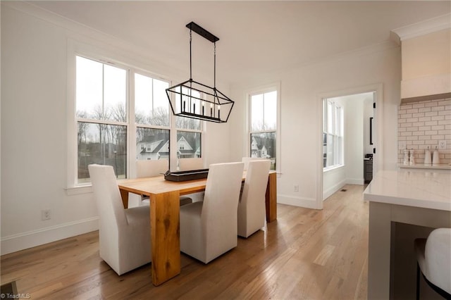 dining space with light wood-type flooring, baseboards, a notable chandelier, and crown molding