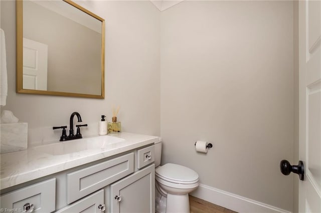 half bathroom featuring vanity, toilet, and baseboards