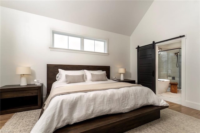 bedroom with ensuite bath, vaulted ceiling, a barn door, and wood finished floors