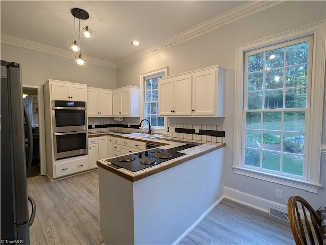 kitchen with appliances with stainless steel finishes, kitchen peninsula, white cabinetry, and pendant lighting