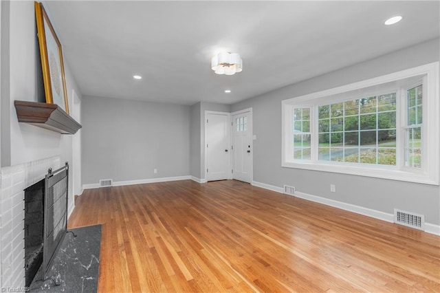 unfurnished living room with light wood-type flooring and a brick fireplace