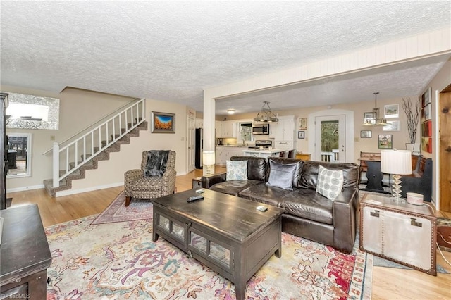 living room featuring stairway, a textured ceiling, light wood-type flooring, and baseboards