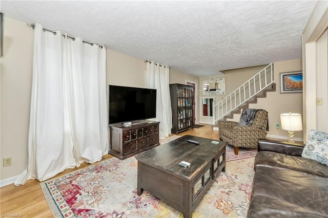 living room with a textured ceiling, stairs, baseboards, and wood finished floors