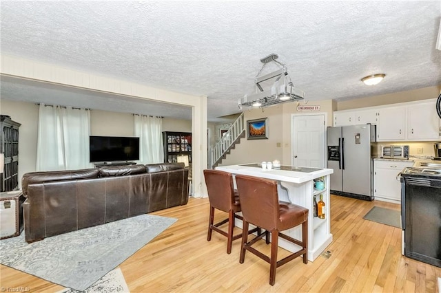 kitchen featuring light wood-type flooring, light countertops, white cabinets, stainless steel fridge, and a textured ceiling